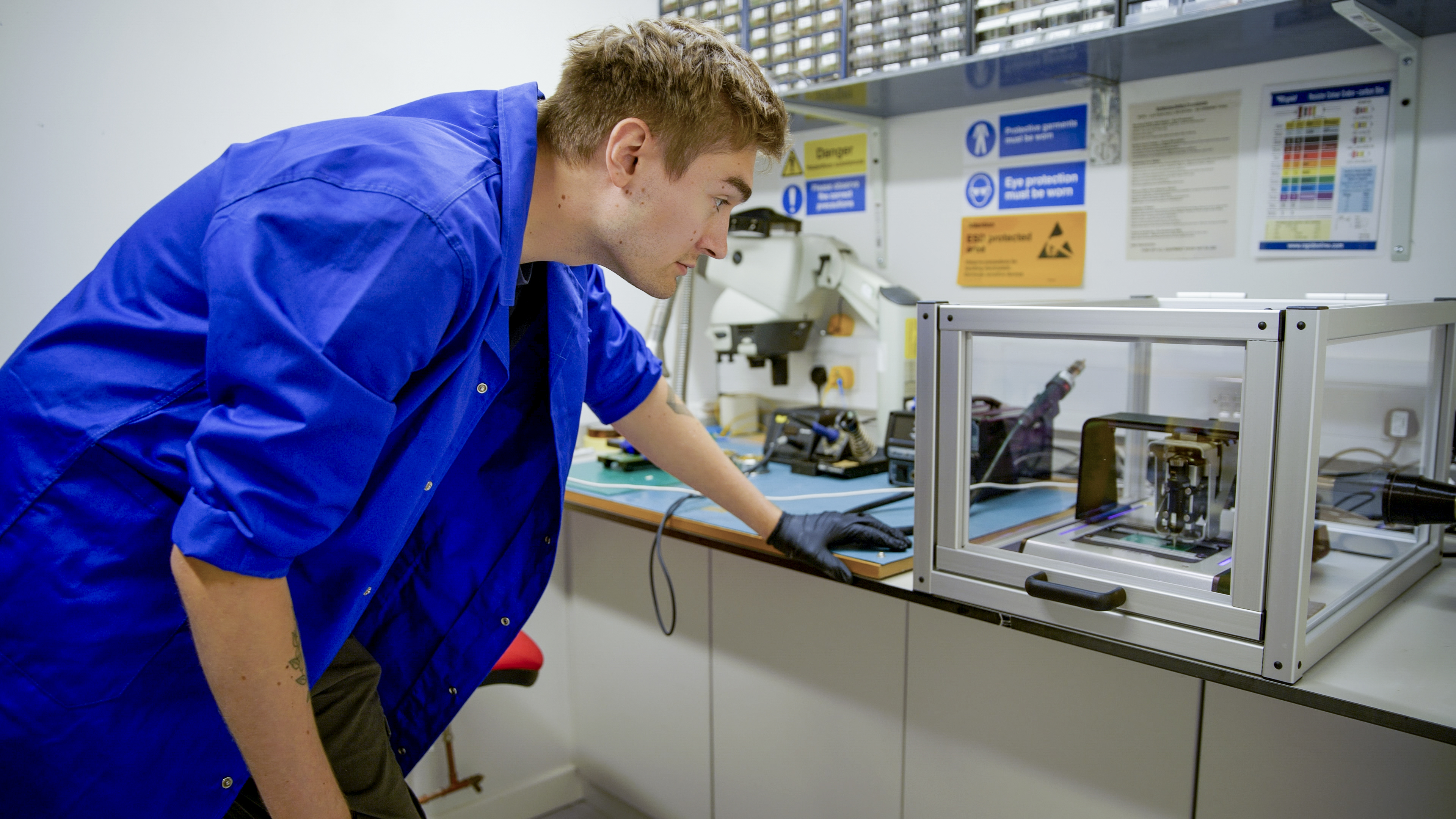 Person in a blue lab coat looking a glass box